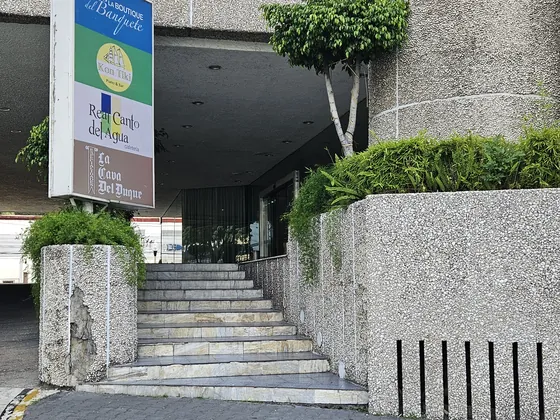 Escalera de piedra de la entrada de personas del hotel, con el tótem que anuncia La Boutique del Banquete, Kon Tiki, Real Canto del Agua y La Cava del Duque