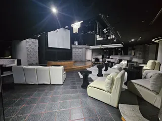 Sillones blancos frente a la tarima de duela, con la pantalla de proyección al fondo