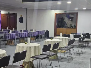 Mesas redondas con mantel morado y crema, sillas alrededor y puertas de madera al fondo