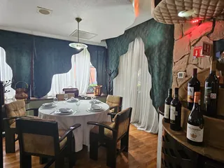 Mesa redonda de La Cava del Duque, vestida con mantel blanco, copas y servilletas dobladas, entre la cortina verde y la columna de piedra