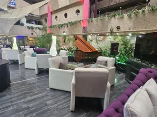 Butacas blancas del Kon Tiki con el piano de cola al fondo, entre las plantas y las velas de tela