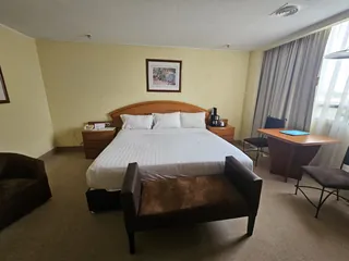 Habitación Ejecutiva: cama King con cabecera de madera, banca al pie y cortinas