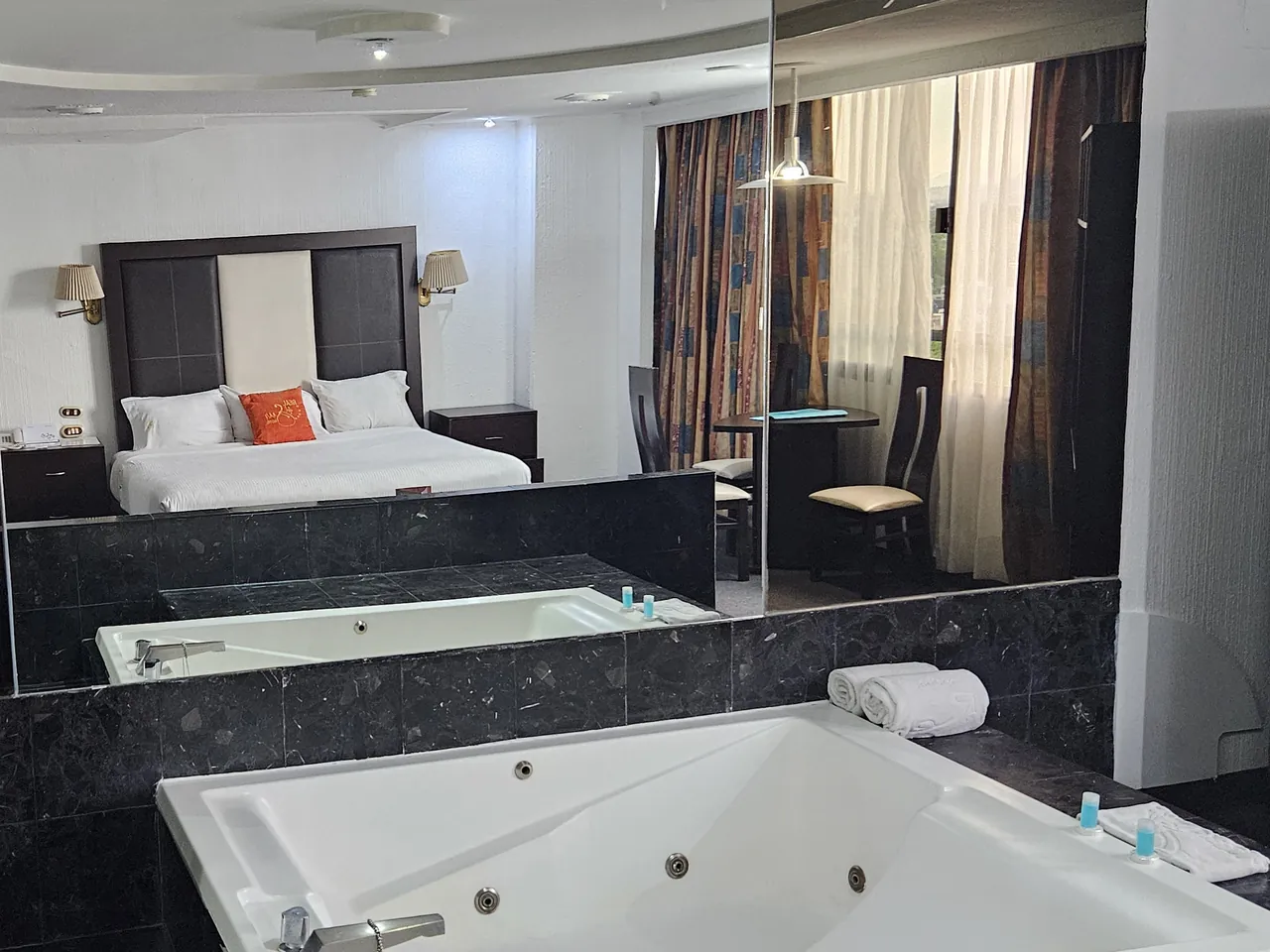 Jacuzzi de una suite del Hotel Real del Sur sobre plataforma de mármol negro, con las toallas dobladas en el borde y la recámara reflejada en el espejo