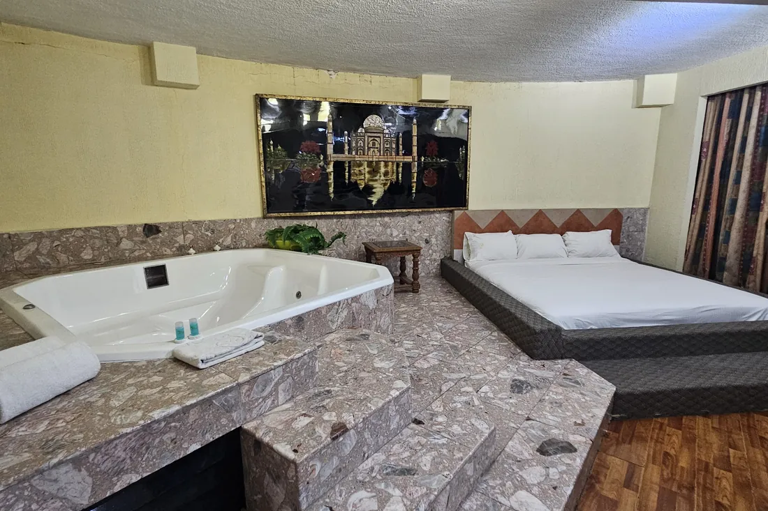 Jacuzzi de la Suite Presidencial sobre plataforma de piedra, con las toallas dobladas en el borde y la cama al fondo